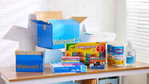 A desk with Walmart shipping boxes, crayons, hand sanitizer, and sanitizing wipes.